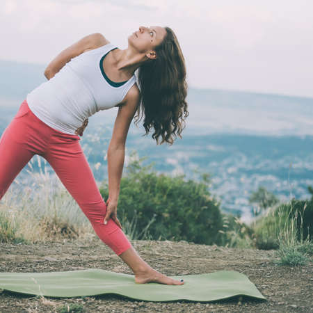Young woman practicing yoga outdoor in the nature with city on background. Toned imageの写真素材