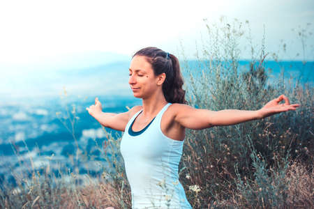 Young woman spreading hands wide open with city on background. Freedom concept. Love and emotions, woman happiness. Toned imageの写真素材
