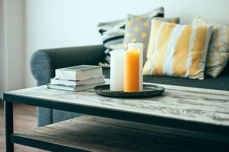 Modern wooden coffee table and cozy sofa with pillows. Living room interior and home decor concept. Toned image