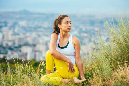 Young woman sits in yoga pose with city on background. Freedom concept. Calmness and relax, woman...