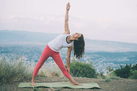 Young woman practicing yoga outdoor in the nature with city on background. Toned imageの写真素材