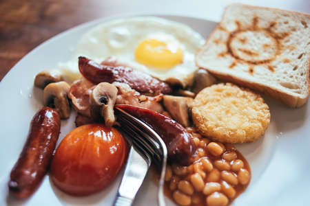 Traditional English breakfast with bacon, sausage, mushrooms, tomatoes, fried egg, hash browns and baked beans. Served with toastの写真素材