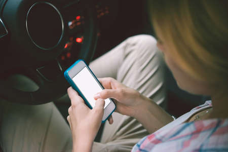 Young woman looks at her smartphone in a car. Toned image