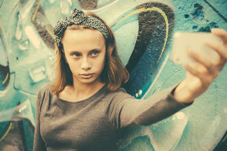 A teenage girl takes selfie with graffiti in the background. Toned imageの写真素材