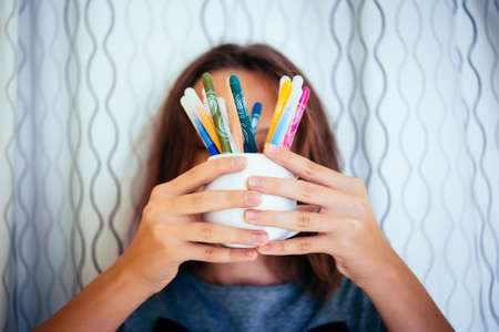 A teenage girl holds a glass with color pencils or pensの写真素材