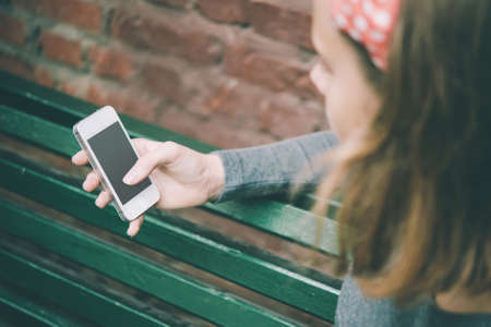 A teenage girl looks at her smartphone with brick wall in the background. Toned imageの写真素材