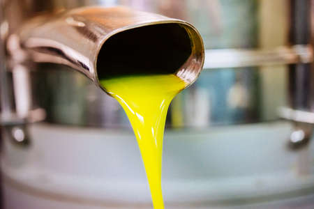 Oil is pouring from the tube at a cold-press factory after the olive harvesting in one of the sicilian villages, Italyの写真素材
