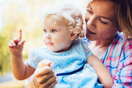 Young beautiful mother with her toddler blonde daughter during a walk outdoors. Toned image