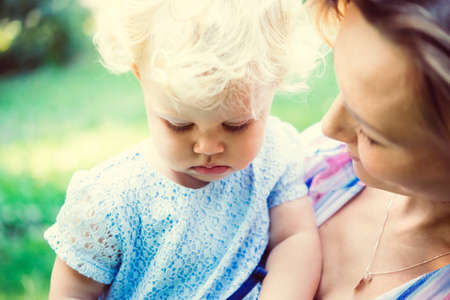 Young beautiful mother with her toddler blonde daughter during a walk outdoors. Toned imageの写真素材