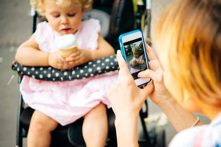 Mother takes a photo of her daughter eating ice-cream during a walk outdoorsの写真素材