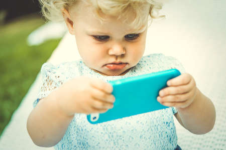 Portrait of cute blonde baby girl with smartphone. Toned imageの写真素材