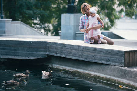 Mother and daughter feed the ducks during a walk outdoors. Toned imageの写真素材