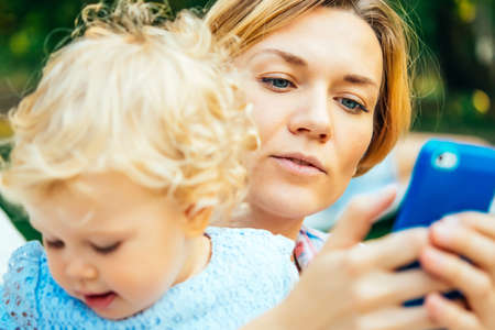 Young beautiful mother checks messages on her smartphone during a walk outdoorsの写真素材