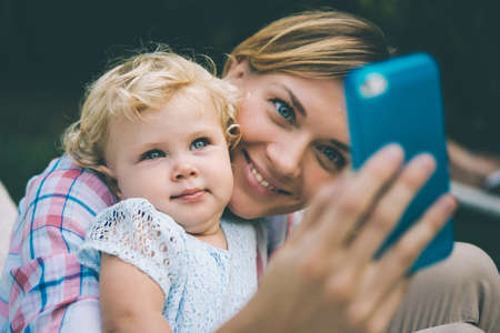 Young beautiful mother takes selfie with her daughter during a walk outdoors. Toned imageの写真素材