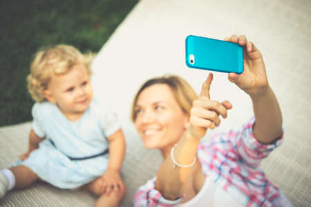 Mother points to her smartphone to take a selfie with her daughter . Toned imageの写真素材