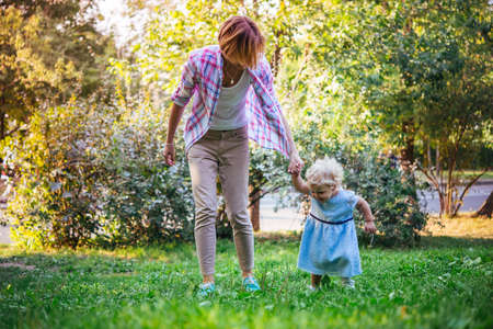 Young beautiful mother walks with her toddler blonde daughter in parkの写真素材