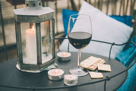 Glass of wine and candles on small iron table on the terrace or balcony. Toned pictureの写真素材