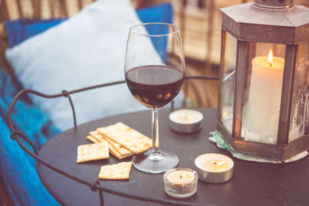 Glass of wine and candles on small iron table on the terrace or balcony. Toned pictureの写真素材
