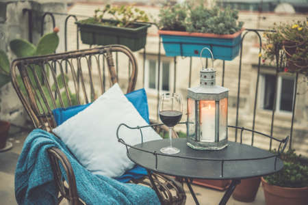Beautiful terrace or balcony with cozy rattan armchair and wine glass on small iron table. Toned pictureの写真素材