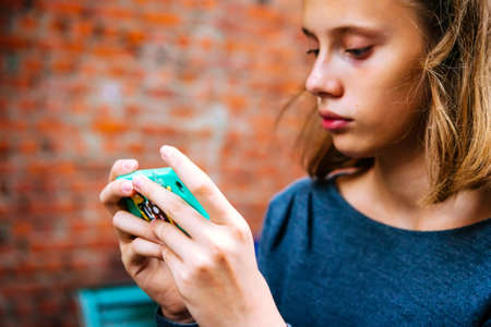 A teenage girl looks at her smartphone with brick wall in the backgroundの写真素材