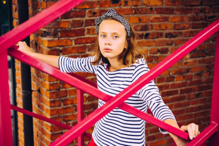 A portrait of a teenage girl posing at the stairs with brick wall in the backgroundの写真素材