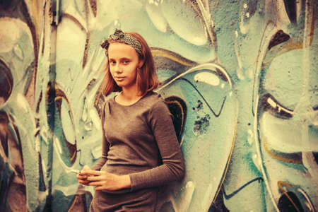 A teenage girl with smartphone leaning against the wall with graffiti. Toned imageの写真素材