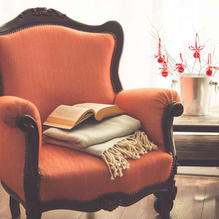 Book, cup and warm plaid on cozy retro armchair. Christmas or new year decoration concept. Toned pictureの写真素材