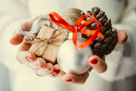 Woman's hands hold christmas or new year decoration. Small gift box, glass ball and cone. Toned pictureの写真素材