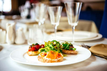 Plate of assorted Italian appetizer bruschetta with chopped vegetables, salmon and meat on ciabatta bread, garnished with green mix saladの写真素材