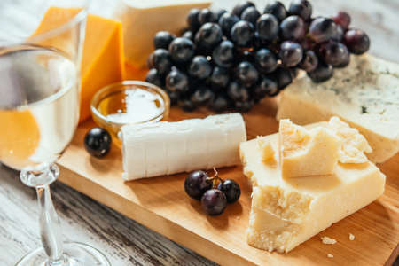 Different types of cheese with grape on wooden board served with the glass of white wine. Toned imageの写真素材