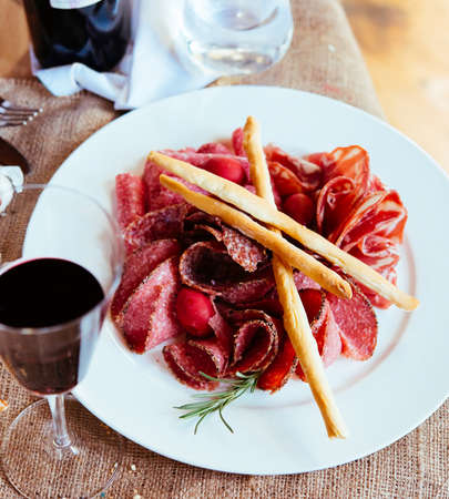 Appetizers or tapas - sausage, meat and salami - on white plate with glass of wineの写真素材