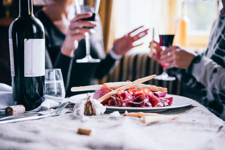 Restaurant or bar table with plate of appetizers and wine. Two people talking on background