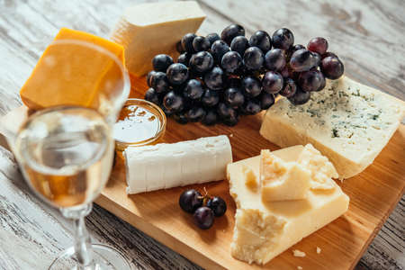 Different types of cheese with grape on wooden board served with the glass of white wine. Toned imageの写真素材