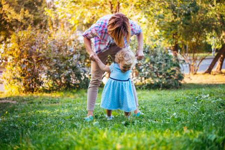 Young beautiful mother walks with her toddler blonde daughter in parkの写真素材