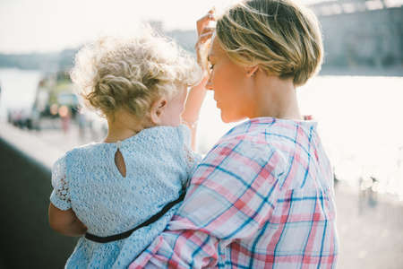 Young beautiful mother with her toddler blonde daughter during a walk outdoors. Toned imageの写真素材