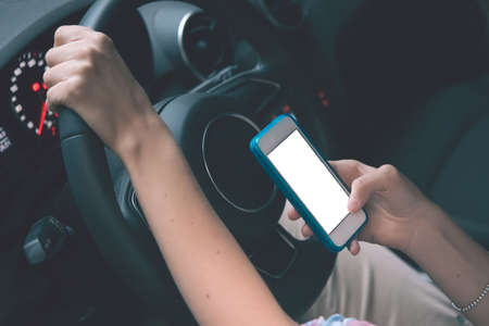 Young woman looks at her smartphone while driving car. Toned imageの写真素材