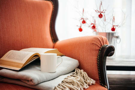 Book, cup and warm plaid on cozy retro armchair. Christmas or new year decoration conceptの写真素材