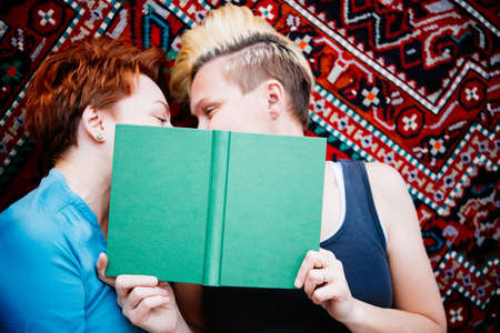 Cute lesbian couple read together lying on the carpet. Selective focus on bookの写真素材