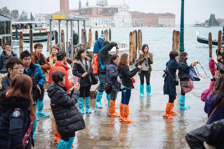 VENICE, ITALY - OCTOBER 14, 2015: Tourists wearing rain boots walk around San Marco square in rainy weather in Venice, Italy.のeditorial素材