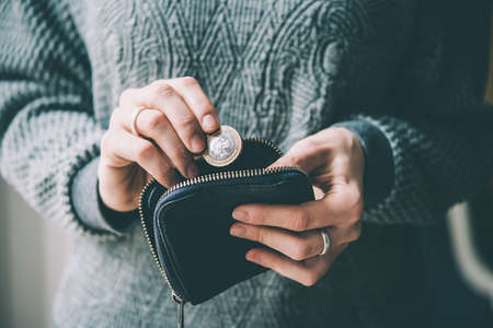 Hands holding british pound coin and small money pouch. Toned picture