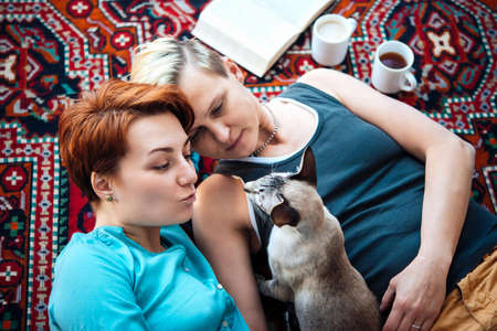 Cute lesbian couple cuddle their pet on the carpetの写真素材