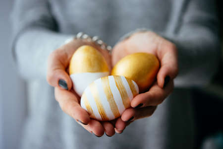 Hands holding modern  easter eggs painted in goldの写真素材