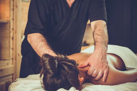 Woman enjoying relaxing back massage in cosmetology spa centre. Beauty treatment, body care, skin care, wellness, wellbeing concept. Toned pictureの写真素材