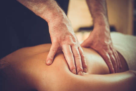 Woman enjoying relaxing back massage in cosmetology spa centre. Beauty treatment, body care, skin care, wellness, wellbeing concept. Toned pictureの写真素材