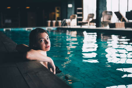 A young beautiful woman swims in a pool. Wellness concept. Calmness and relax, woman happiness. Toned pictureの写真素材
