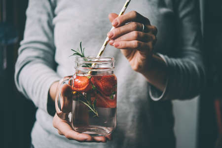 Hands holding retro glass jar of lemonade or cocktail with strawberry and rosemary. Toned pictureの写真素材