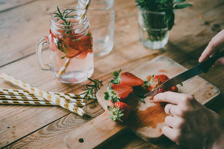 Making of lemonade or cocktail with strawberry and rosemary on wooden table. Toned pictureの写真素材