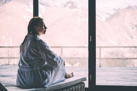 Young beautiful woman is relaxing in a bathrobe after swimming in the pool with mountains view....