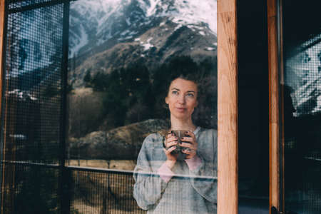Young beautiful woman enjoys her morning tea looking at the mountains. Freedom concept. Calmness and...