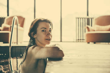 A young pretty woman relaxes in the swimming pool. Wellness concept. Spa and relax, woman happiness. Toned pictureの写真素材